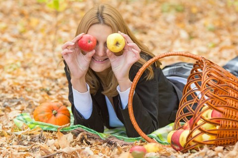 Young beautiful girl lying on the leaves in the autumn forest in the fun and put the apples to the