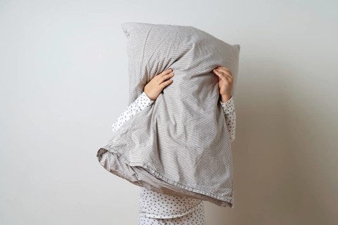 Portrait of pretty caucasian girl in white pyjama and pillow in studio white background .