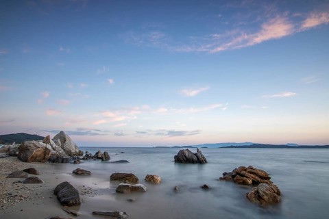 View through rocks on a sandy beach into the sunset. Landscape shot with view to the horizon over