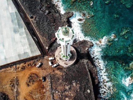 Aerial top view of lighthouse, rocks and ocean waves in a volcanic landscape with lava. Punta Lava