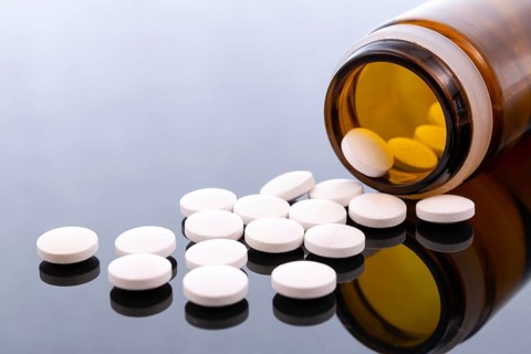 White pills and brown glass bottle isolated on black reflective surface. Global pharmaceutical