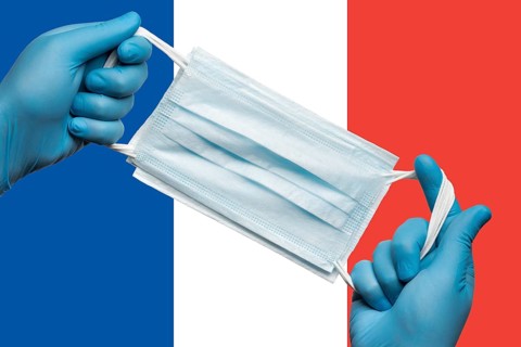 Doctor holding respiratory face mask in hands in blue gloves on background flag flag of France or