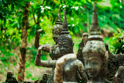 Weathered stone statues amidst green foliage in a forest setting, figures, stone figures,