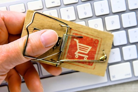 Hand in mousetrap with shopping trolley in front of a computer keyboard, photomontage