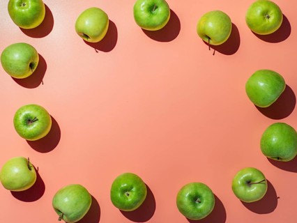 Green apples on orange or coral pink background with copy space for text or design in center,