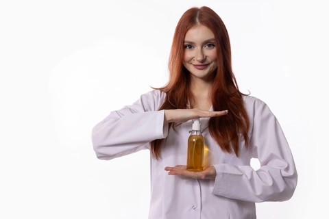 A smiling young woman in a lab coat showcases an innovative hair care product, highlighting beauty