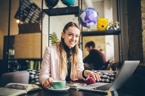 Beautiful young caucasian woman drinking coffee and typing on a keyboard inside a cafe at a wooden