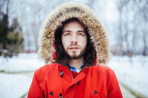 Portrait, close-up of a young stylish man with a beard dressed in a red winter jacket with a hood