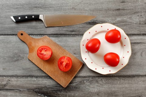 Table top view on three tomatoes on white porcelain plate with red dots, cutting board with tomato