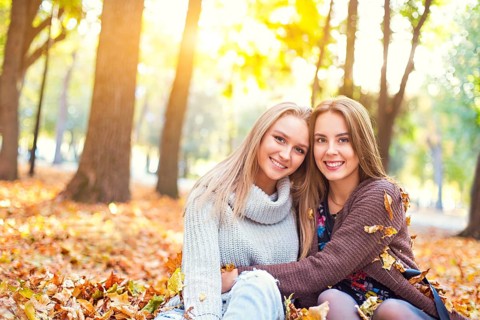 Fashionable beautiful young girlfriends walking together in the autumn park background. Having fun