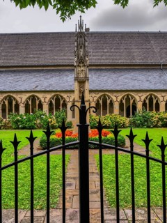 Iron gate in front of a garden in the monastery courtyard with well-tended flowerbeds and Gothic