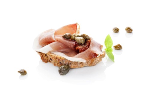 Luxurious canape background. Ciabatta slice with prosciutto, dry tomato and capers isolated on