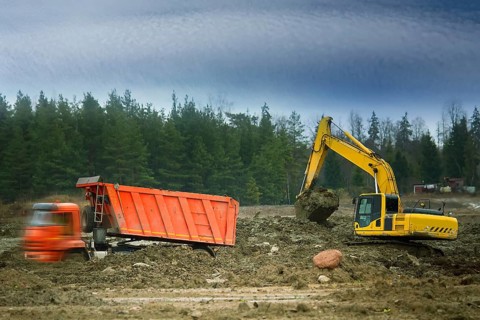 Preparation of the site for construction, leveling the soil. Excavator loads excess soil into