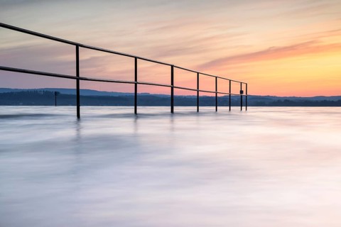 A railing in calm water, surrounded by a pastel-coloured sunrise, lido, Litzelstetten, Lake