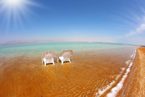 Two white beach chairs stood side by side in the clear water. The sun shines on the beach