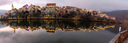 Christmas illuminated house facade of Frohnleiten reflected in the river Mur, panoramic view,