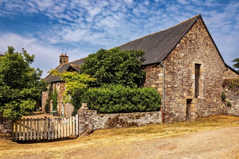 Rural stone house with a small wooden fence and green bushes under a clear sky, The Abbey de La