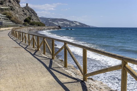 Promenade with wooden railings by the sea in front of the village with blue sky and sea, Castillo