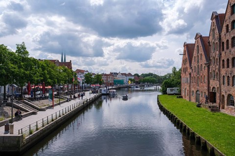 City view with waterway and historic brick buildings, flanked by green areas and clouds, Lübeck,