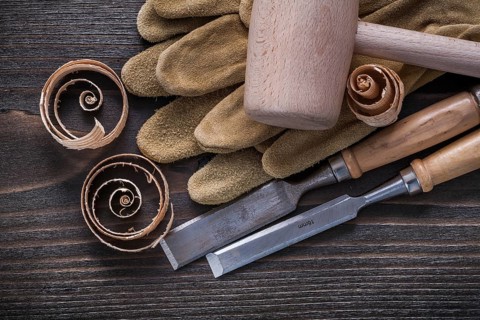 Pair of brown leather gloves firmer chisels wooden hammer and shavings on vintage wood board