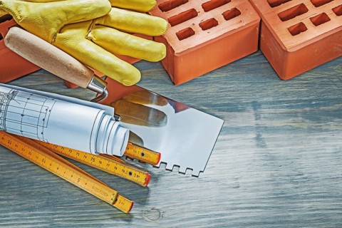 Red bricks working gloves blueprints wooden meter palette plastering trowel on wood board