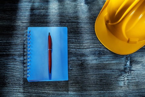 Notepad pen hard hat on wooden board