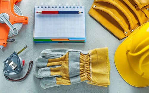 Protective gloves hard hat notepad pencil tool belt measuring tape on concrete background