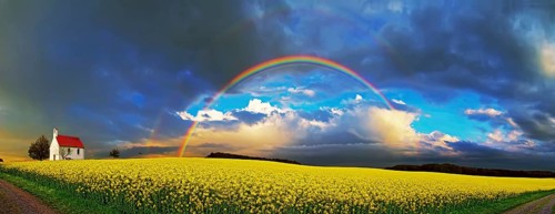 Panorama, chapel and rainbow over a rapeseed field