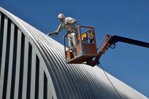 Tradesman spray painting the roof of an industrial building, Greymouth, South Island