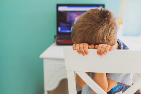 The sad little boy sits in front of laptop and doesn't want to look lesson. Concept of boring