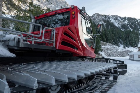 Tracked snow groomer with huge tracks in a winter scenery with the snowy austrian alps and forest