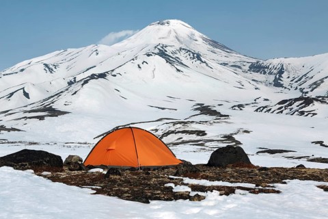 Orange camping (tourist) tent stands on meadow surrounded by snow at foot of beautiful active