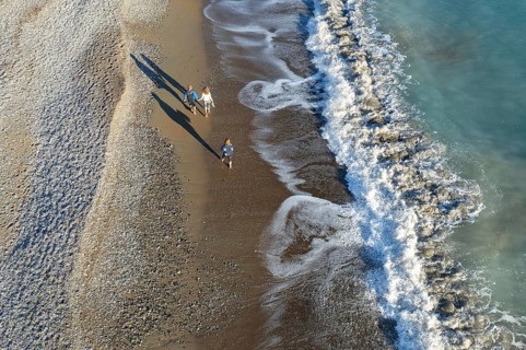 Aerial drone point of view of person walking on sand in a beach. Stormy waves idyllic beach in