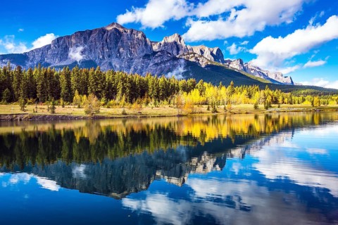 Concept hiking. Canmore, near Banff. Red-orange trees and jagged mountains are reflected in the
