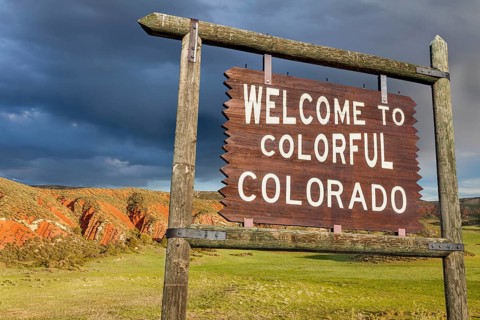 Welcome to colorful Colorado roadside wooden sign with red sandstone cliff in background
