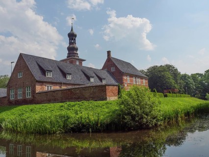 Historic brick building with tower and pond, surrounded by a green garden and blue sky, husum,