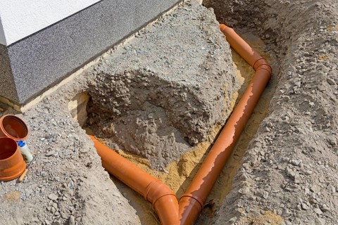Open trench with laid sewage pipes at residential building