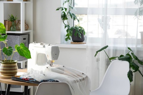 Sewing machine on a round table in the white interior of the house near the window with a