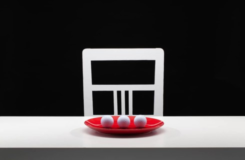 Three white golf balls on the red plate. White old chair and white table in the dark room