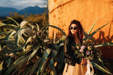 Bride in a beautiful pastel dress and sunglasses holds a bouquet of flowers in her hands against