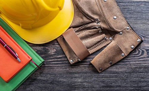 Leather tool belt notepads pen protective building helmet on wooden board construction concept
