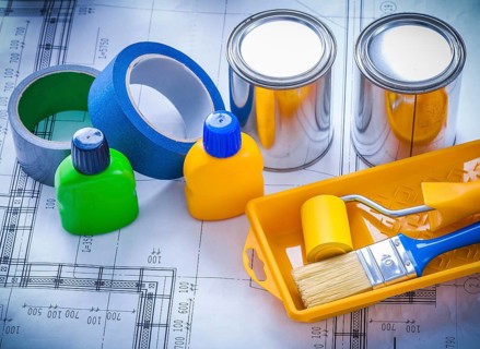 Blueprint with paint brush tray roller cans bottles and household tapes close up image construction