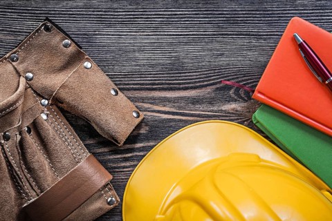 Leather building belt note-books pen yellow hard hat on wooden board top view construction concept