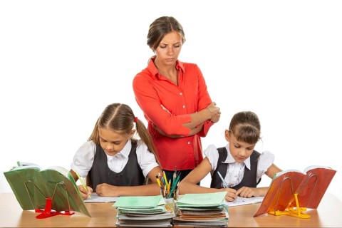 A strict teacher stands above the children who solve the task
