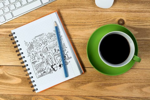 Notepad with idea sketches coffee cup keyboard and pencil on wooden table