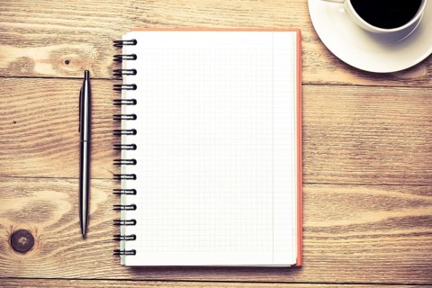 White blank notepad with cup of coffee on wooden table