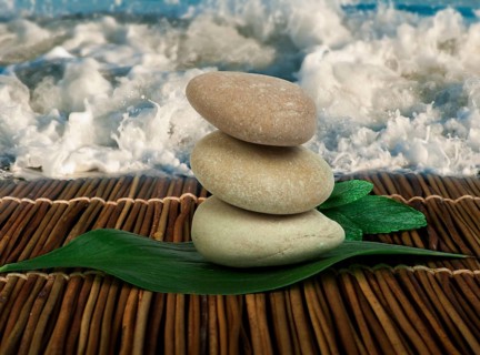 Stacked stones on wooden base for spa and green leafs. Waves on the background