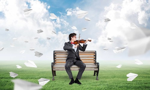 Young businessman plays the violin sitting on a bench, around flying paper planes. Creativity in