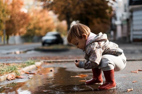 Little girl in red rainboots playing in puddle after rain. Happy fall childhood activity