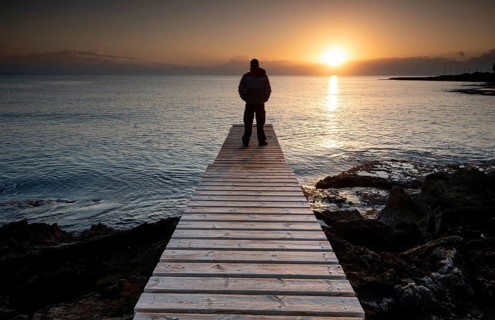 Person standing at the edge of a wooden pier in the sea at sunrise, People active outdoors enjoy
